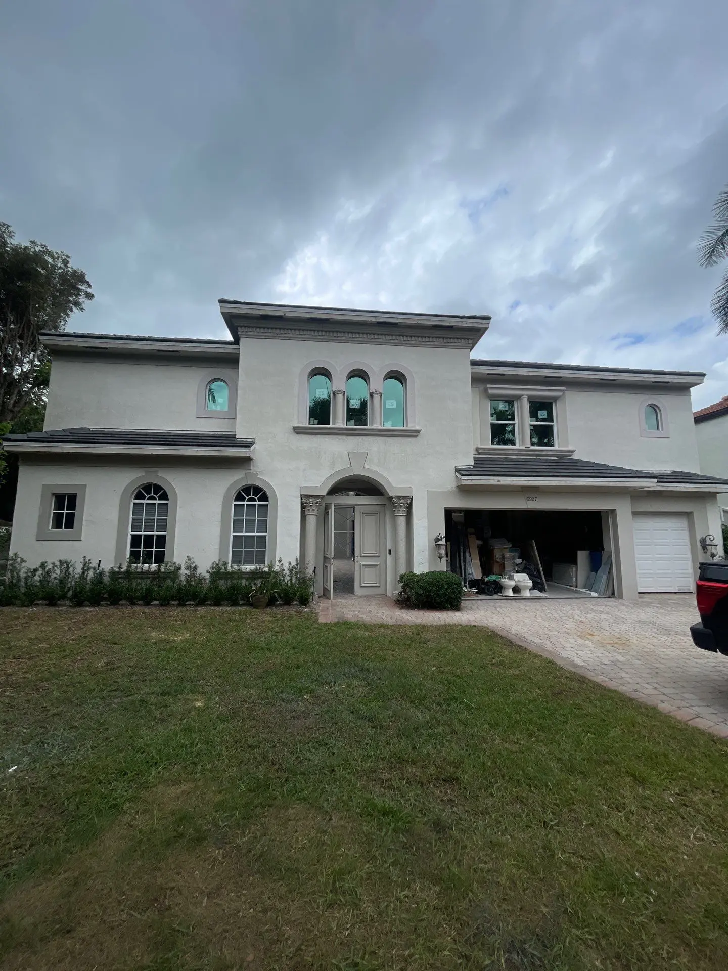 Two-story stucco home with dark tile roof, arched windows, decorative columns and brick paver driveway exterior painting project in Wellington FL