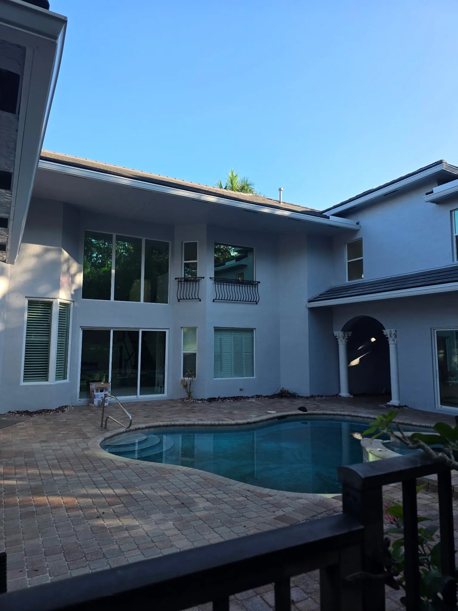 Two-story white stucco home with wrought iron balcony, arched entryway and pool deck exterior painting project in Wellington FL