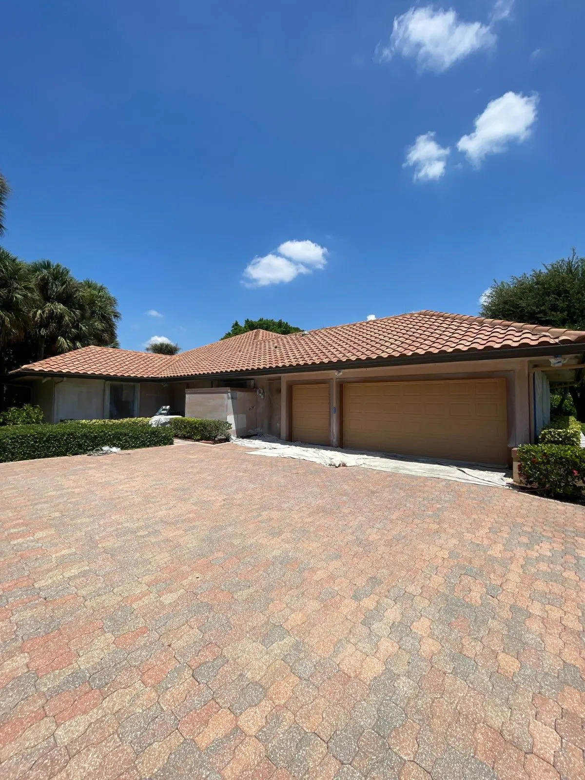 Single-story stucco home with terracotta tile roof, three-car garage and large brick paver driveway mid exterior painting project in Wellington FL