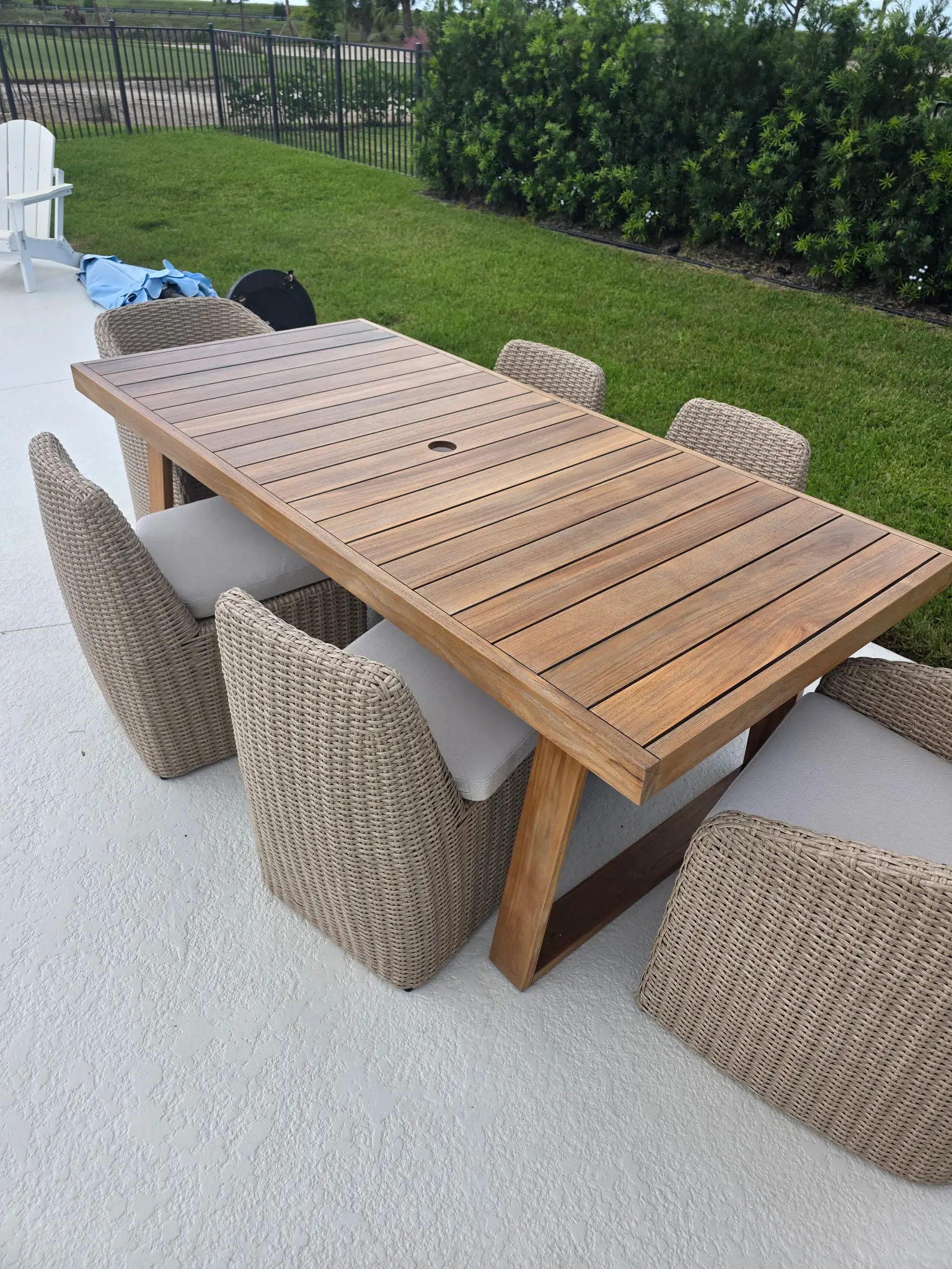 Freshly painted white concrete patio with teak outdoor dining table and wicker chairs overlooking a manicured lawn in Wellington FL
