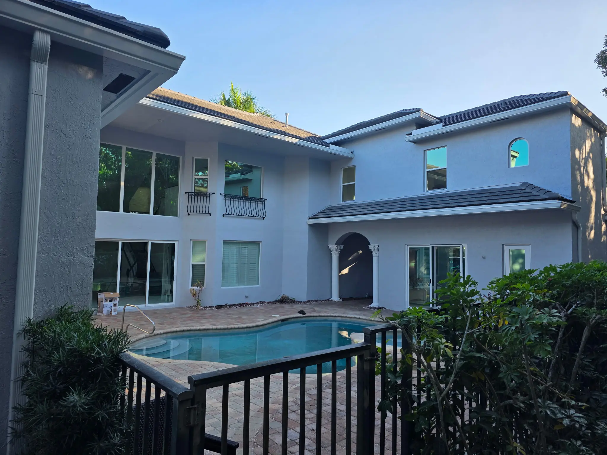 Two-story white stucco home with dark tile roof, wrought iron balcony, arched entryway and pool deck exterior painting project in Wellington FL