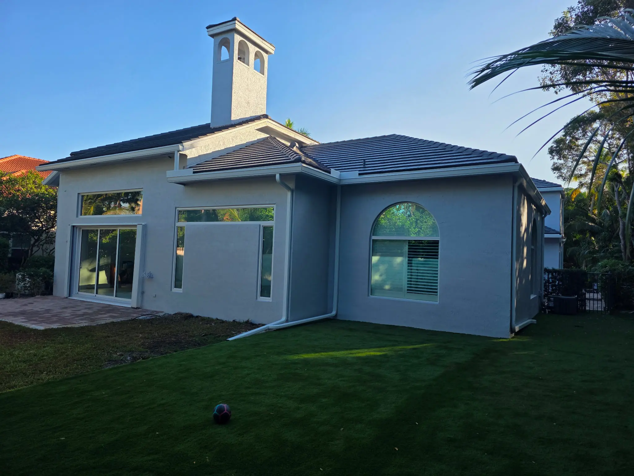 Gray stucco home with dark tile roof, chimney, arched window and manicured lawn exterior painting project in Wellington FL