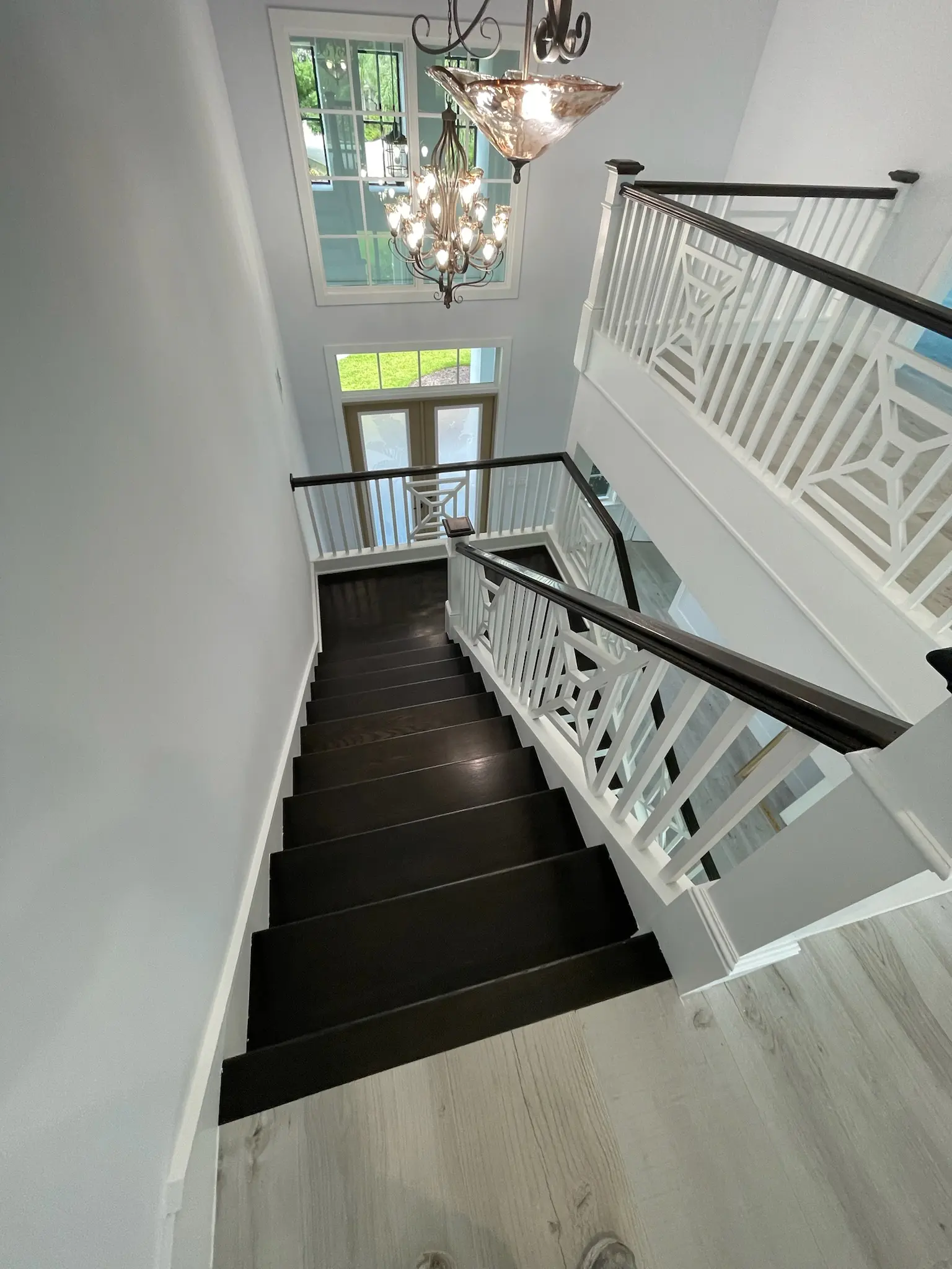 Two-story foyer with freshly painted white walls, dark stained staircase, decorative white balusters and chandelier, interior painting in Wellington, FL