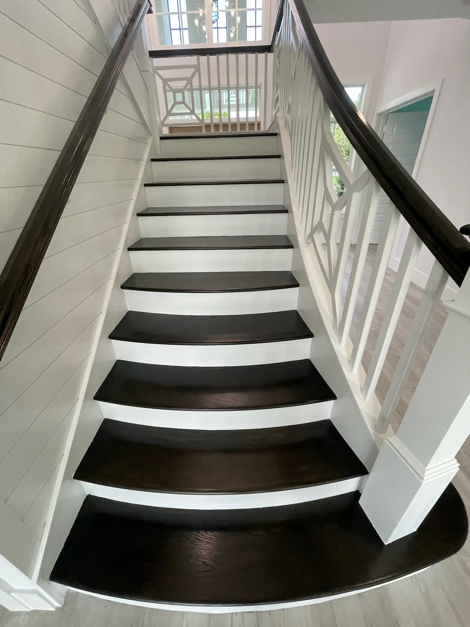 Curved staircase with dark stained wood treads, white painted risers, decorative white balusters and dark handrail, interior painting in Wellington, FL