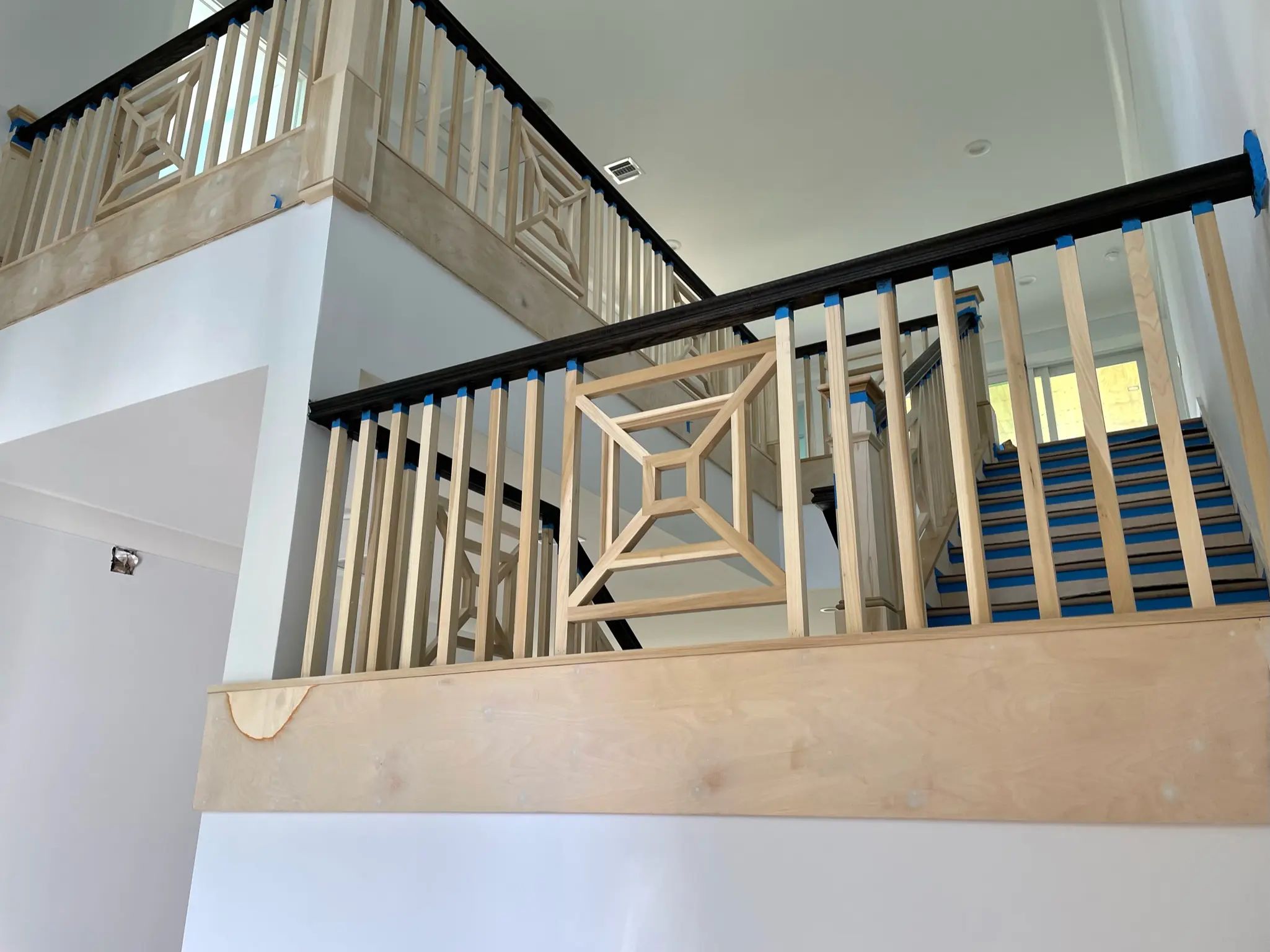 Interior staircase railing with natural wood balusters and decorative panels taped and prepped for painting by Painter Guys