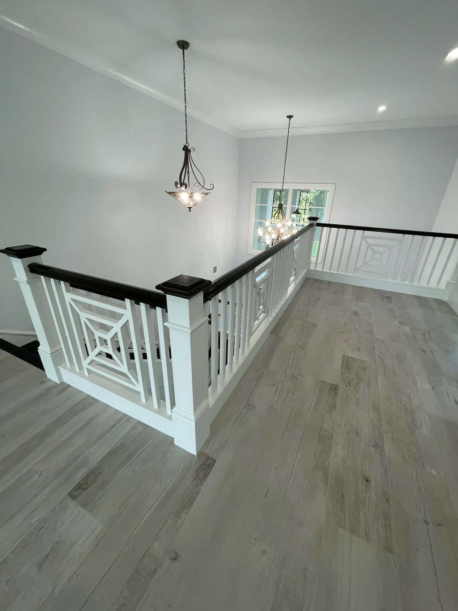 Freshly painted white upper hallway with decorative balusters, dark handrail, pendant lighting and wide plank wood floors, interior painting in Wellington, FL