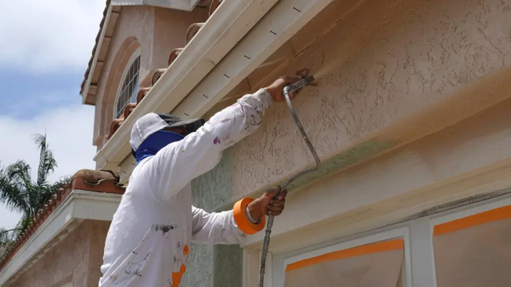 Painter applying exterior paint to a stucco home in Palm Beach County, Florida.