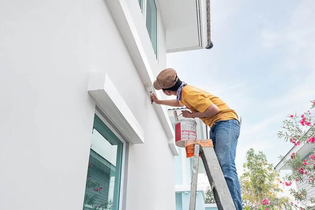 Painter on a ladder painting the exterior of a residential home in Palm Beach County, Florida.