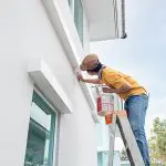 Painter on a ladder painting the exterior of a residential home in Palm Beach County, Florida.