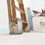 Professional painter with roller and paint bucket preparing to paint interior walls of a home.